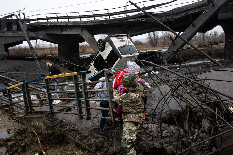 A Ukrainian soldier is helping civilians to cross the Irpin river over a destroyed bridge, March 2022